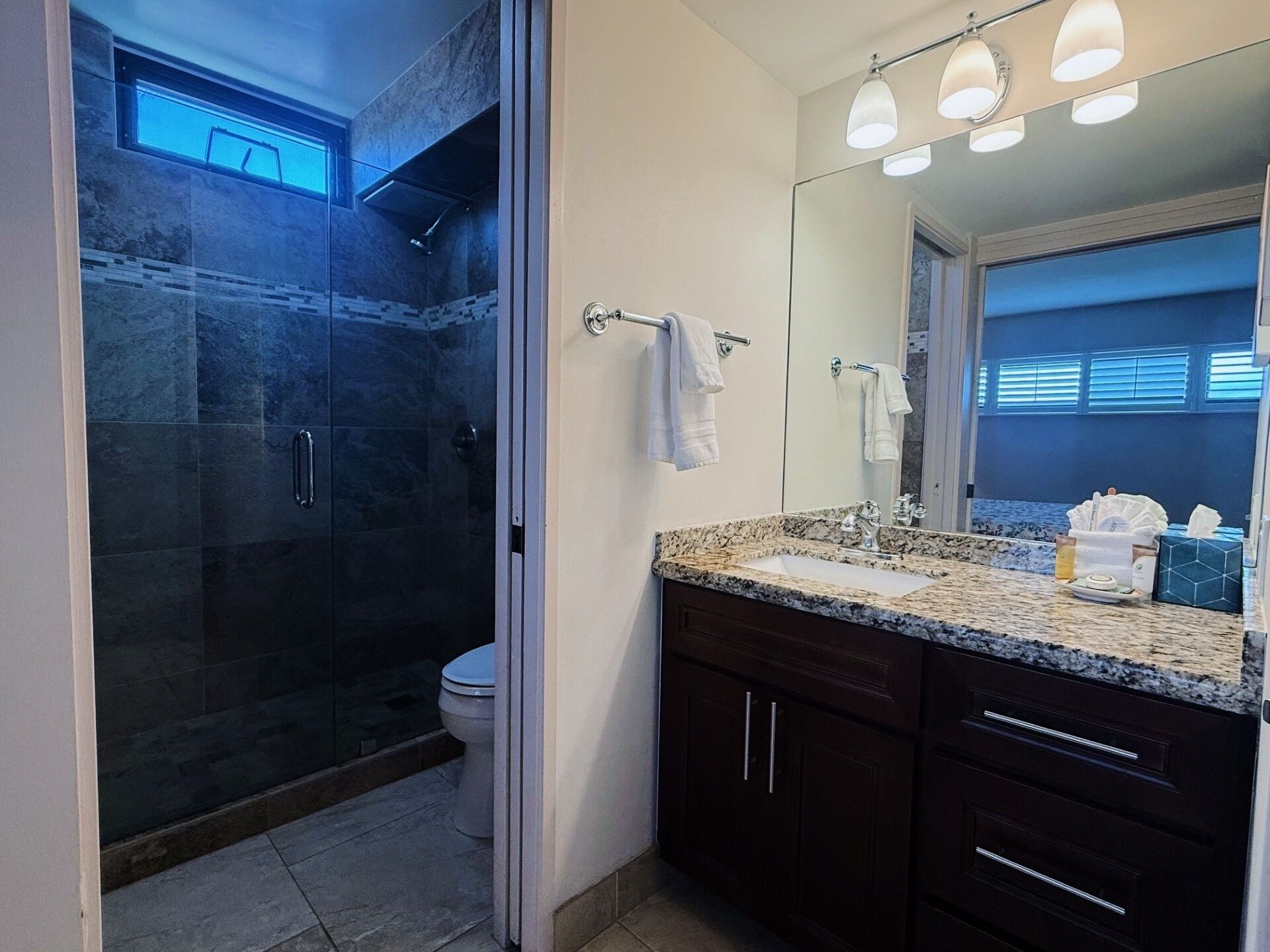 Un bagno moderno con doccia vetro, un mobile lavabo con piano in granito e uno specchio grande.