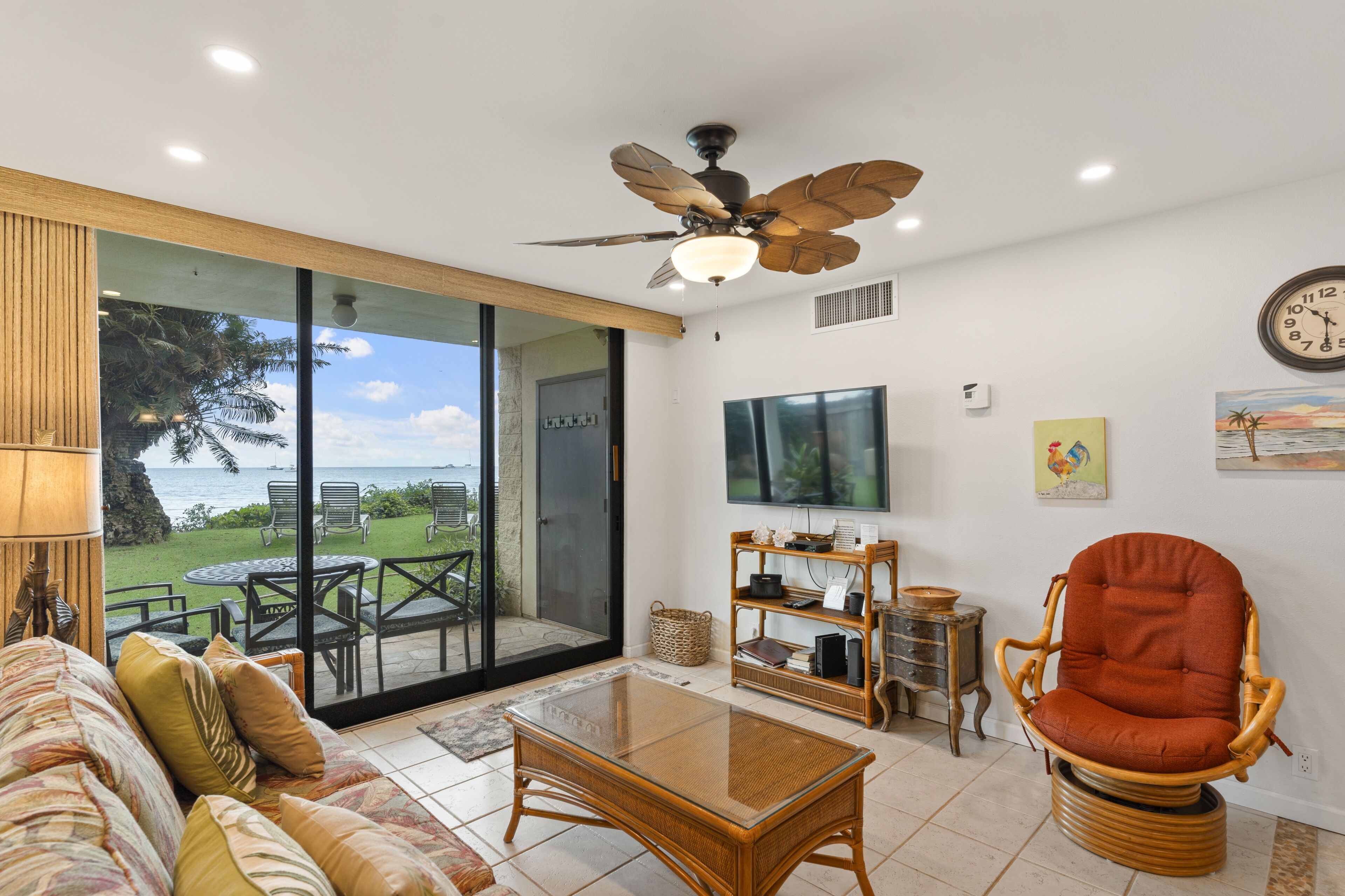 A living room with a glass door leading to a patio, a ceiling fan, a flat-screen TV, and a wicker chair.