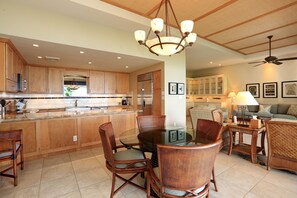 A spacious kitchen with wooden cabinets, a central island, and a dining area with wicker chairs and a glass table.