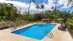 A rectangular swimming pool with a clear blue water surface, surrounded by lounge chairs and umbrellas, with palm trees and a clear sky in the background. - Makena Surf, #f-202 2 Bedroom Condo by RedAwning (Kihei)