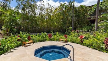 Uma banheira de hidromassagem rodeada por vegetação tropical exuberante e um banco de madeira.