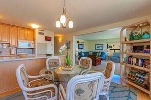 A modern kitchen with a microwave, a whiteboard, and a dining area with wicker chairs and a glass table. - Sugar Beach Resort, #ph12 2 Bedroom Condo by RedAwning (Kihei)