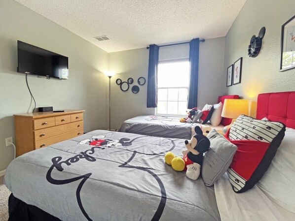 Un dormitorio con dos camas, un televisor montado en la pared, un aparador y una ventana con cortinas.