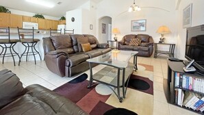 A spacious living area with leather sofas, a glass coffee table, and a TV. There is a kitchen in the background with wooden cabinets and a microwave. - Park Villa 4 Bedroom Villa by RedAwning (Davenport)