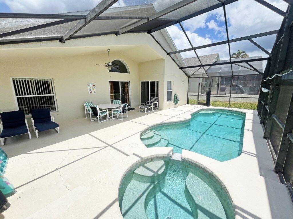 Una piscina exterior techada con techo de vidrio, rodeada de sillones de descanso y una mesa.