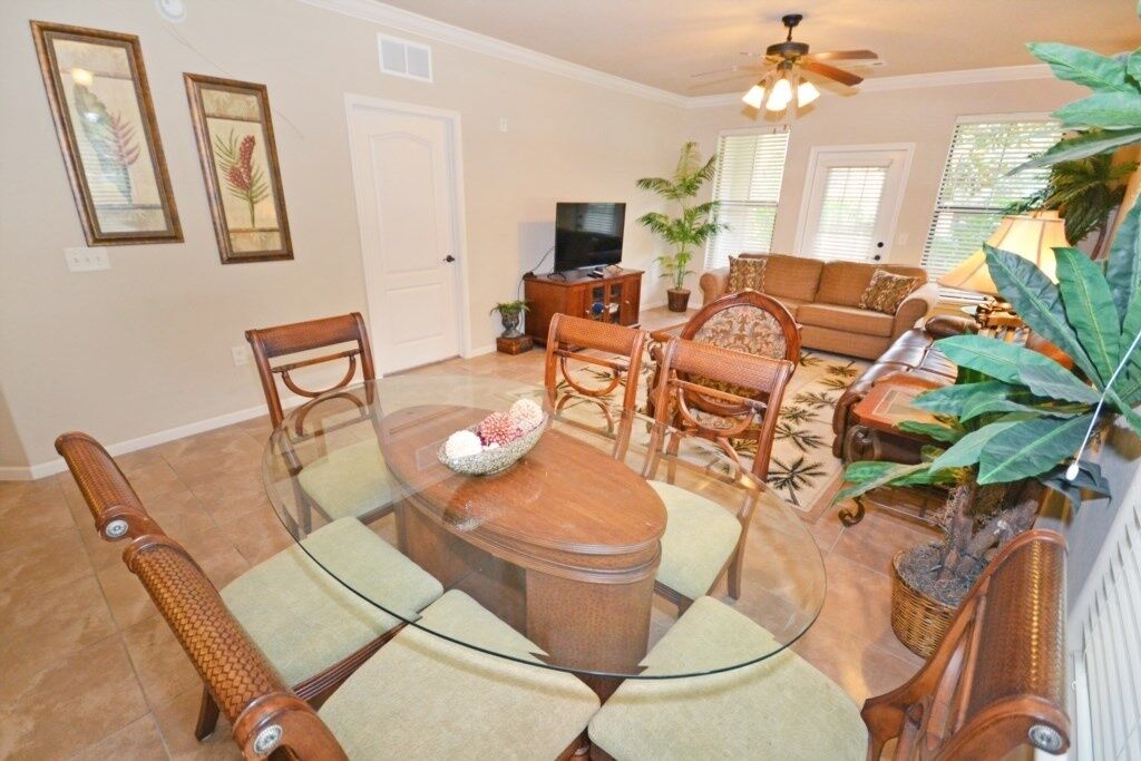 A living room with a glass-top dining table surrounded by wooden chairs, a sofa, and a television.