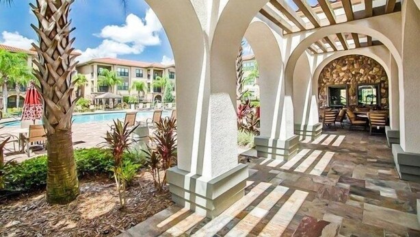 A covered outdoor area with a pool, palm trees, and a stone-tiled floor.
