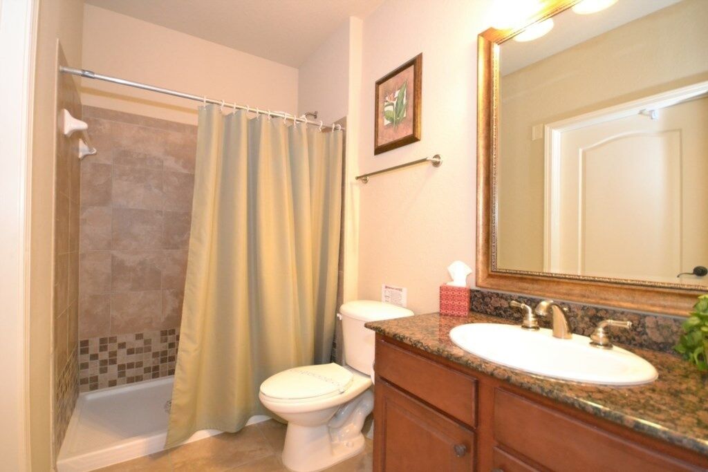 A bathroom with a shower, toilet, sink, and a large mirror.