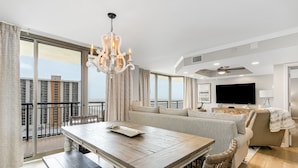 Uma sala de estar espaçosa com uma mesa de jantar grande, um conjunto de sofás, uma televisão e uma varanda com vista para a cidade.