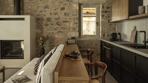 A kitchen with a stone wall, wooden beams, a built-in stove, and a window.