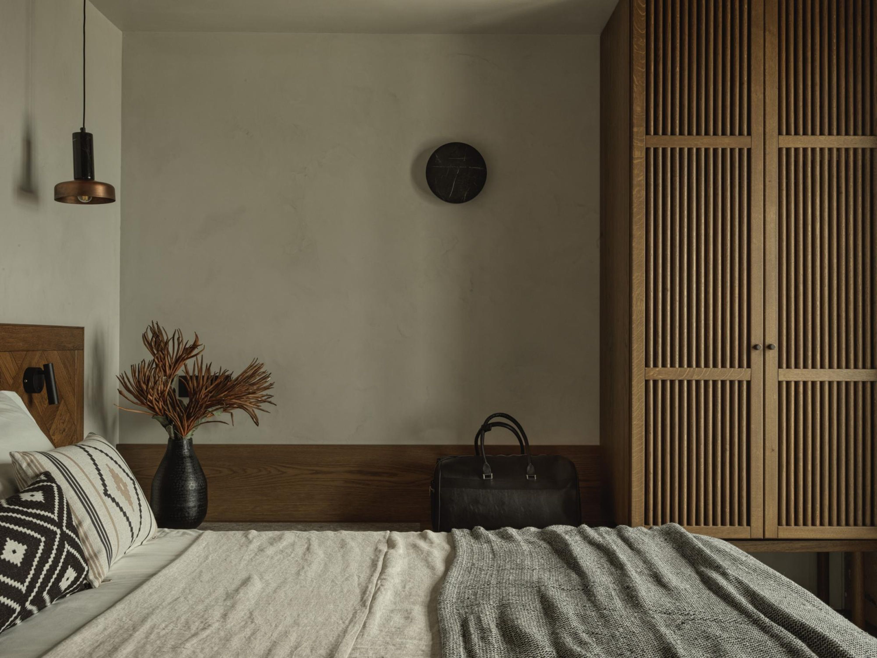 Une chambre à coucher comprenant un lit, une table de chevet, un vase avec des plantes séchées, une horloge au mur et une armoire.