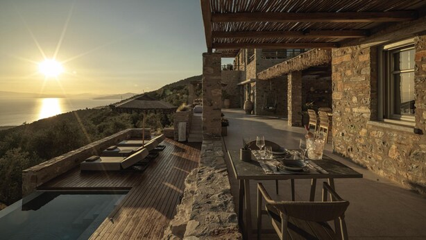 A terrace with a dining table set for two, overlooking a body of water and a mountainous landscape.