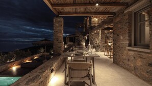 A stone patio with a table and chairs, overlooking a pool and a scenic view.