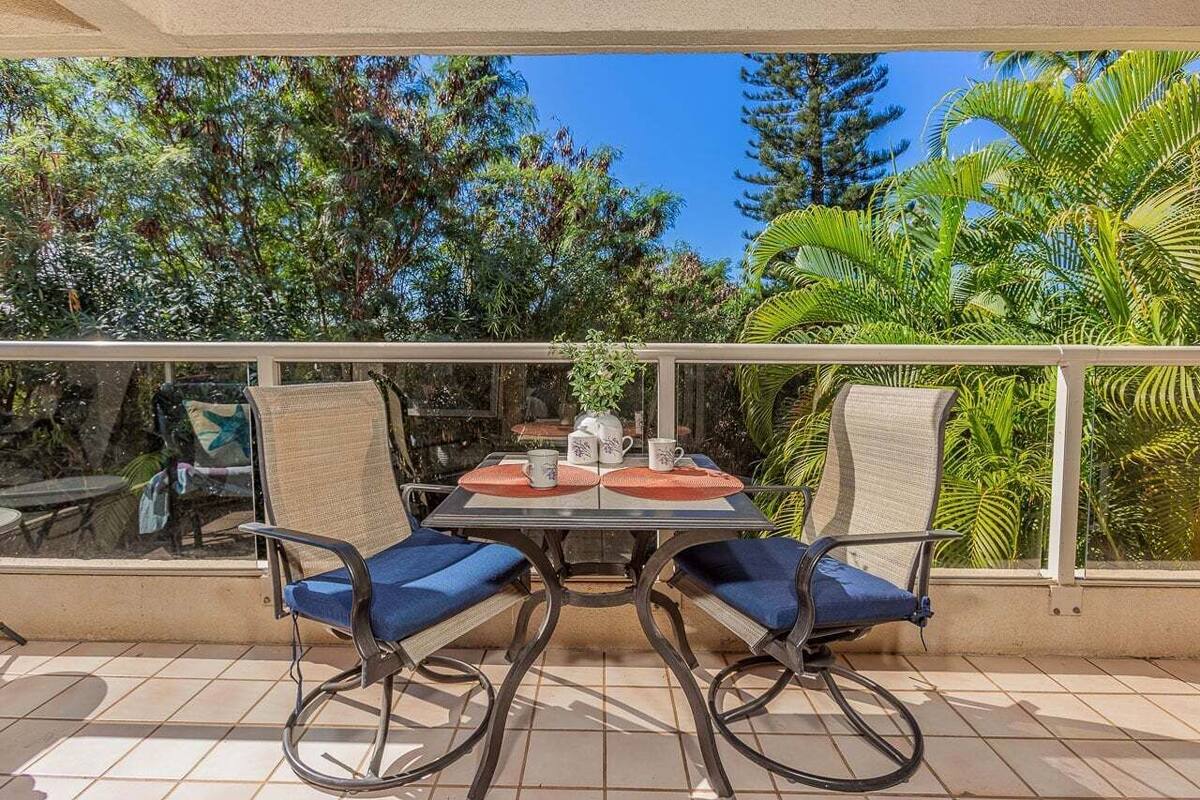 Ein Balkon mit zwei Stühlen und einem Tisch, umgeben von Glasgeländern, mit Blick auf einen tropischen Garten.