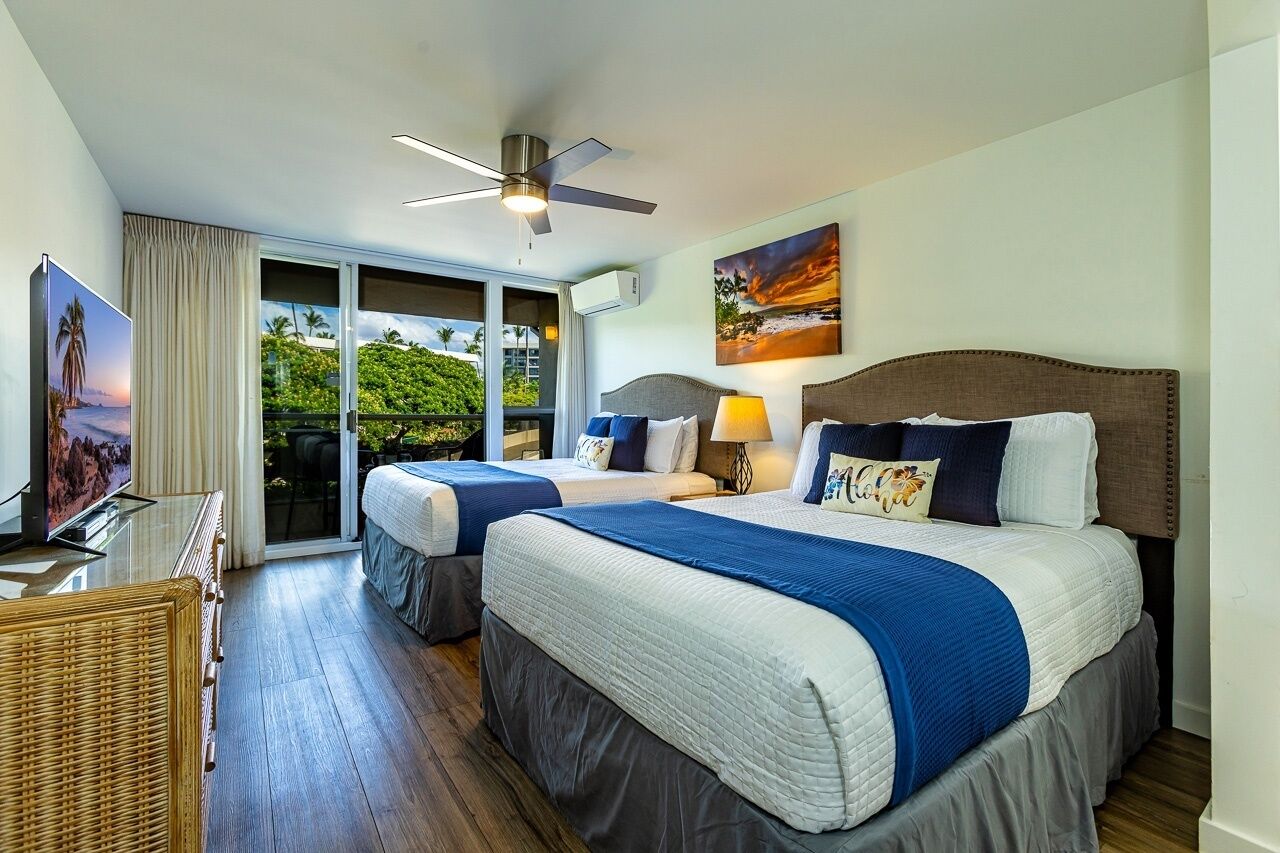 Une chambre d’hôtel avec deux lits, un ventilateur de plafond, une télévision et un balcon donnant sur un paysage verdoyant.