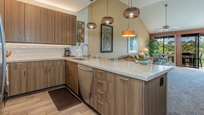 Una cocina moderna con armarios de madera, una isla central, iluminación colgante y vistas al exterior.