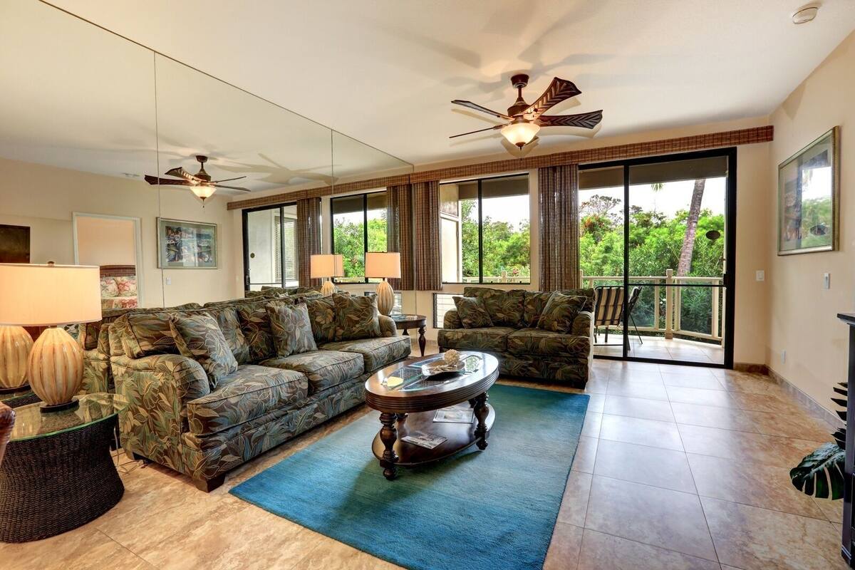 Ein geräumiges Wohnzimmer mit einem großen Sofa, einem Couchtisch und zwei Deckenventilatoren.