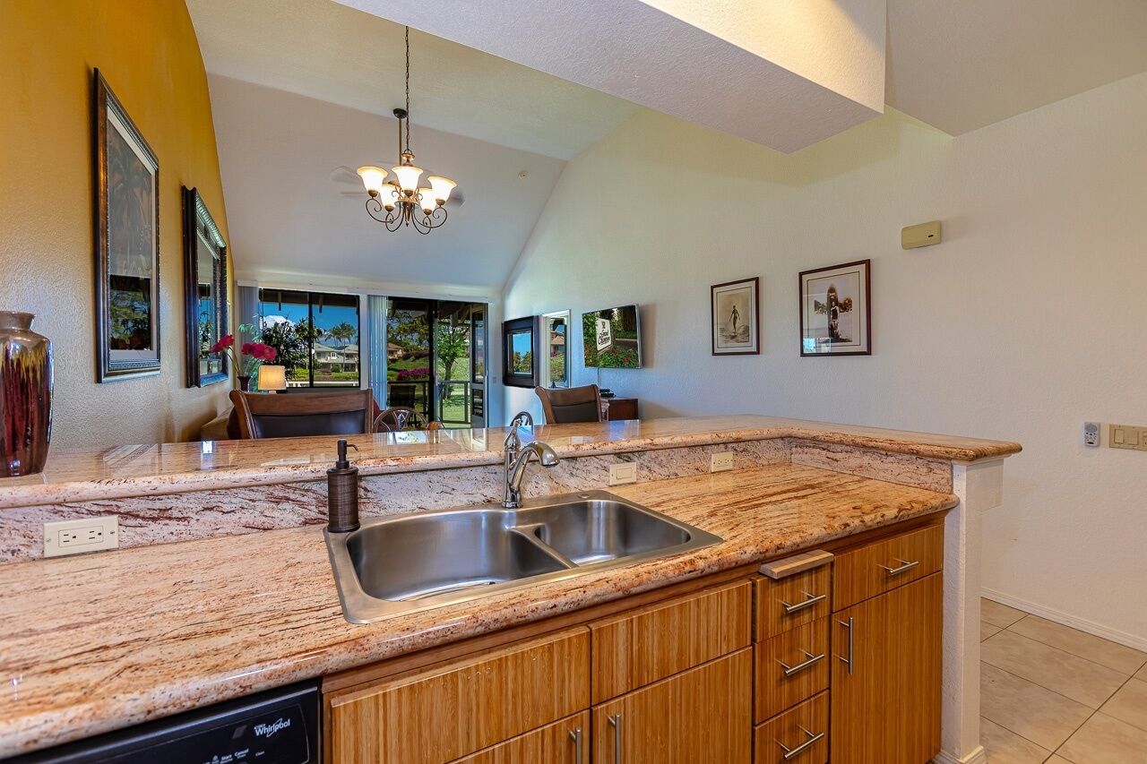 A kitchen with granite countertops, a double sink, wooden cabinets, and a chandelier.