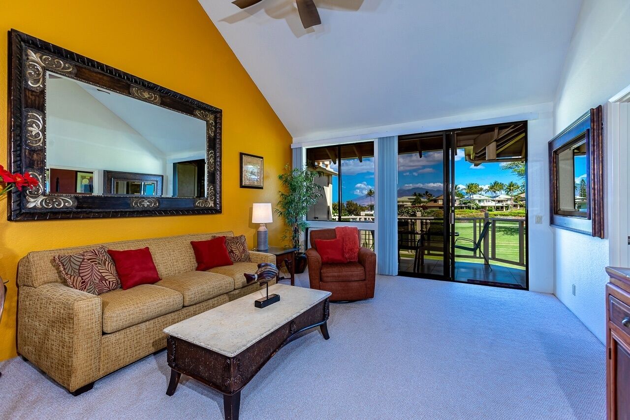 A spacious living room with a yellow wall, a large mirror, a sofa with red cushions, a coffee table, and a chair.