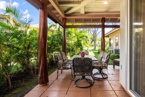 A covered patio with a table and chairs, surrounded by lush greenery.