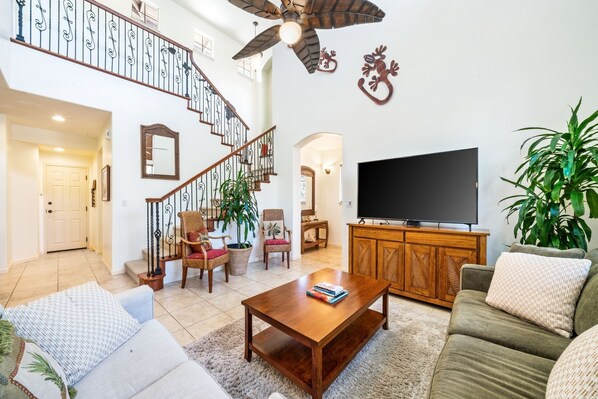 A spacious living room with a staircase, a flat-screen TV, and comfortable seating.