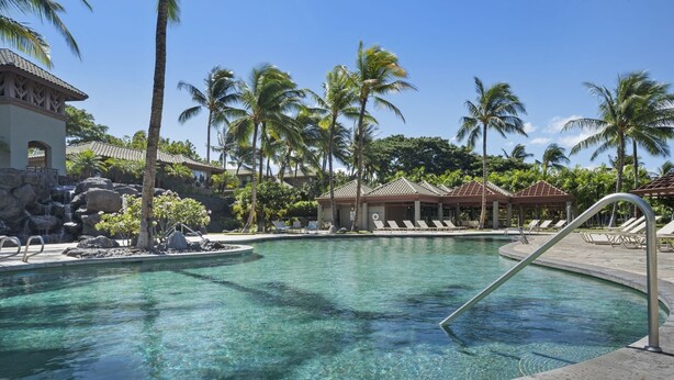 A clear pool with a waterfall feature, surrounded by palm trees and lounge chairs. - Big Island Fairways At Mauna Lani 1701 2 Bedroom Condo (Kamuela)