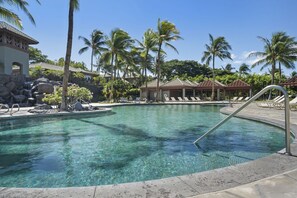 A clear pool with a waterfall feature, surrounded by palm trees and lounge chairs.