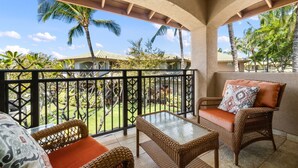 A balcony with wicker furniture and a glass table, overlooking a tropical garden with palm trees. - Big Island Fairways At Mauna Lani 1701 2 Bedroom Condo (Kamuela)