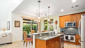 A modern kitchen with granite countertops, wooden cabinets, stainless steel appliances, and pendant lighting. - Big Island Fairways At Mauna Lani 1701 2 Bedroom Condo (Kamuela)