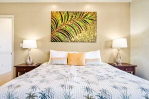 A bedroom with a bed, two bedside tables with lamps, a large painting on the wall, and a floral-patterned bedspread.