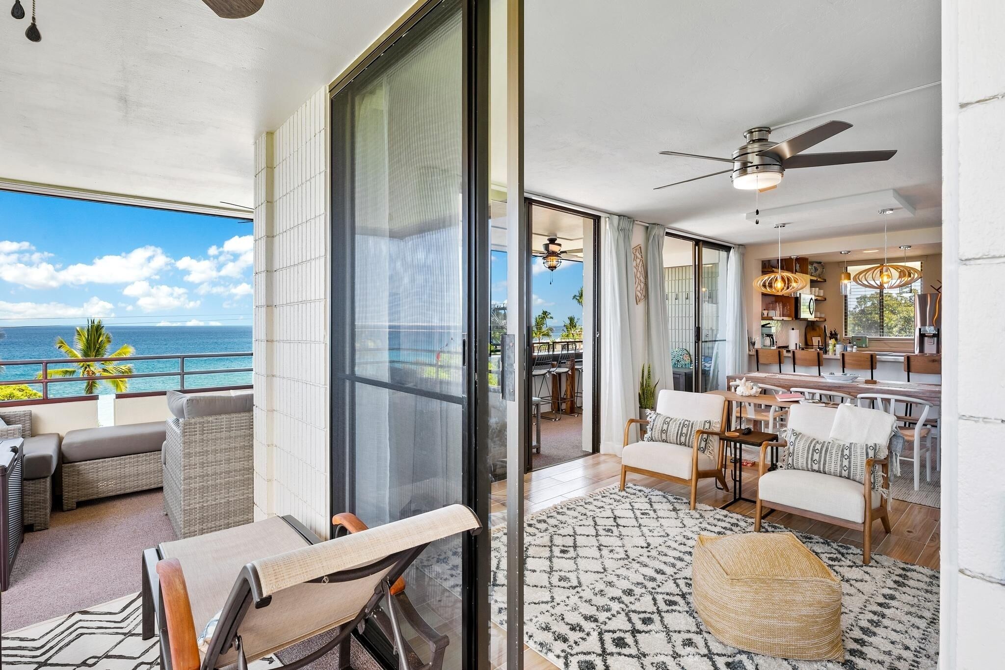 A spacious balcony with a view of the ocean, a dining area with modern furniture, and a kitchen with a bar.