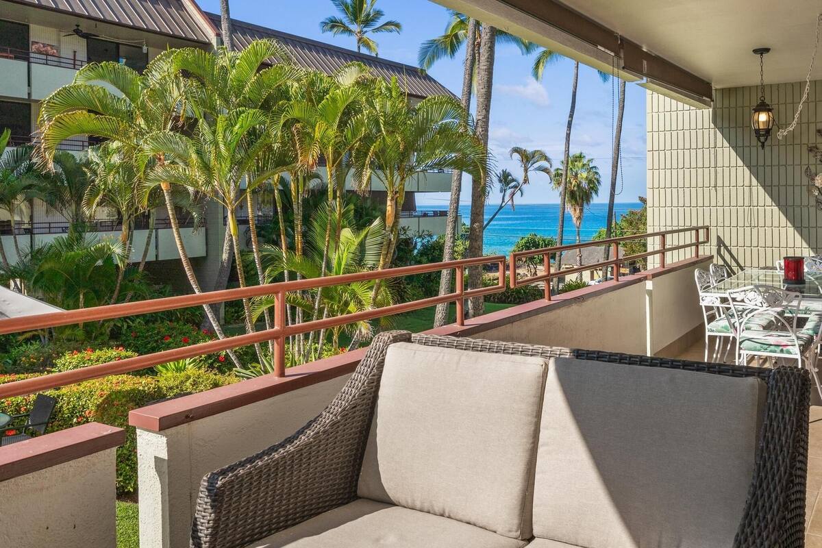 Ein Balkon mit Korbmöbeln, einem Geländer und Blick auf das Meer und Palmen.