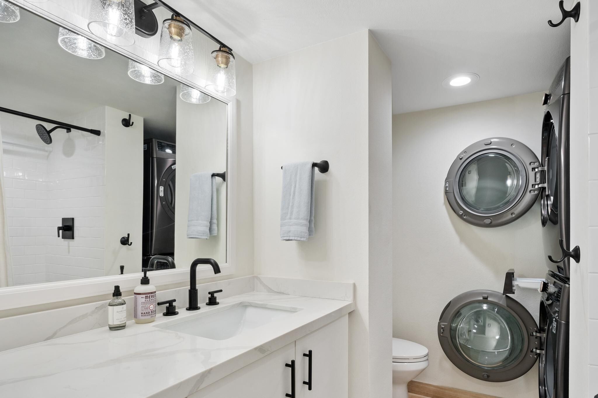 Un baño moderno con un espejo grande, un lavamanos, un inodoro y una lavadora.