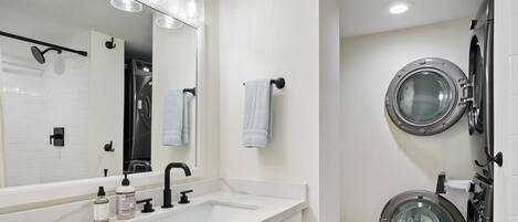 Un baño moderno con un espejo grande, un lavamanos, un inodoro y una lavadora.