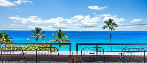 A balcony with metal chairs overlooking a clear blue ocean with palm trees.