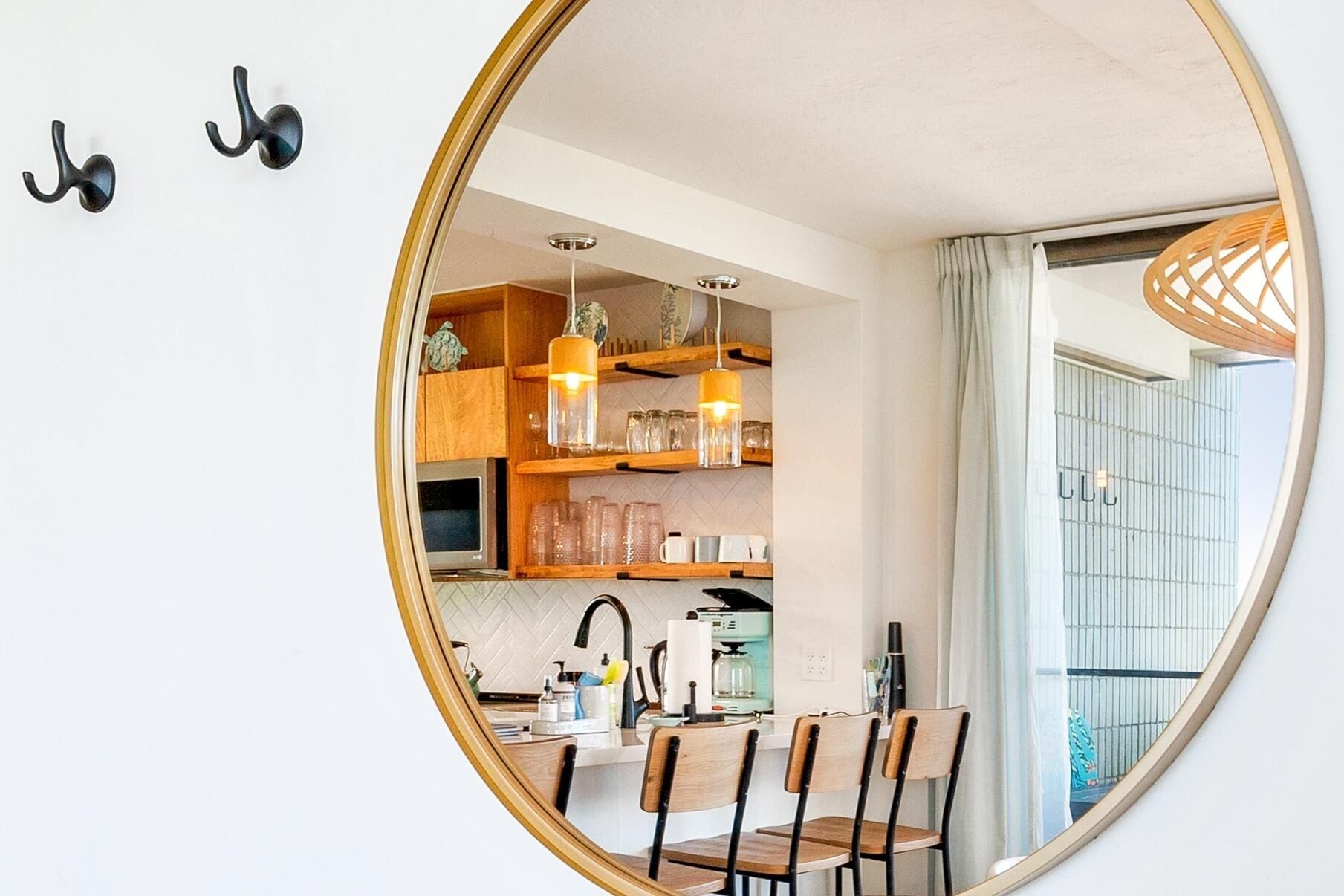 Cocina con armarios de madera, zona de comedor con sillas y un espejo redondo que refleja el ambiente.
