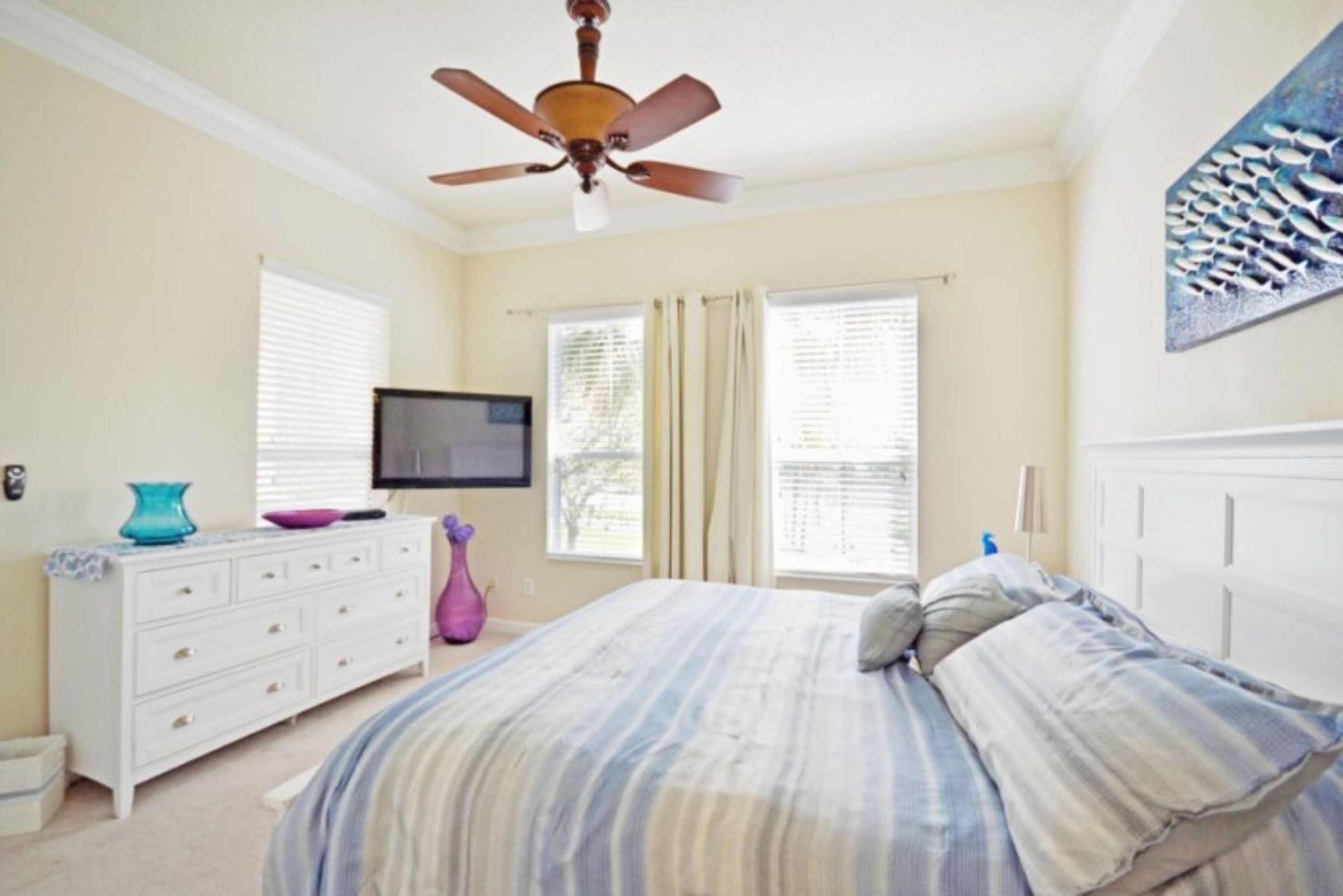 A bedroom with a bed, a dresser, a television, and a ceiling fan.