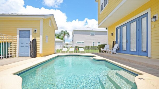 A swimming pool with clear water, surrounded by yellow buildings with blue doors and windows. - Reunion Retreat 3 Bedroom Home by RedAwning (Kissimmee)
