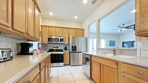 A modern kitchen with wooden cabinets, stainless steel appliances, and a tiled floor. - Reunion Retreat 3 Bedroom Home by RedAwning (Kissimmee)