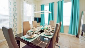 A dining area with a glass table, six chairs, and teal curtains. - Reunion Retreat 3 Bedroom Home by RedAwning (Kissimmee)