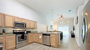 A modern kitchen with wooden cabinets, stainless steel appliances, and a large island. - Sunshine Villa 5 Bedroom Villa by RedAwning (Kissimmee)