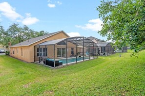 A house with a large glass-enclosed patio area, a swimming pool, and a well-maintained lawn. - Sunshine Villa 5 Bedroom Villa by RedAwning (Kissimmee)
