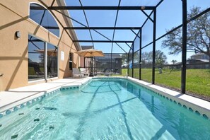 A swimming pool with a glass enclosure, surrounded by a patio area with lounge chairs and an umbrella. - Sunshine Villa 5 Bedroom Villa by RedAwning (Kissimmee)