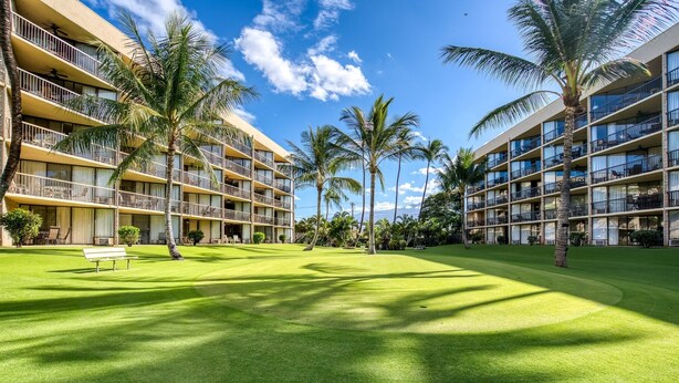 A hotel with multiple balconies, a well-maintained lawn, and palm trees. - Maui Sunset B309 1 Bedroom Condo (Kihei)