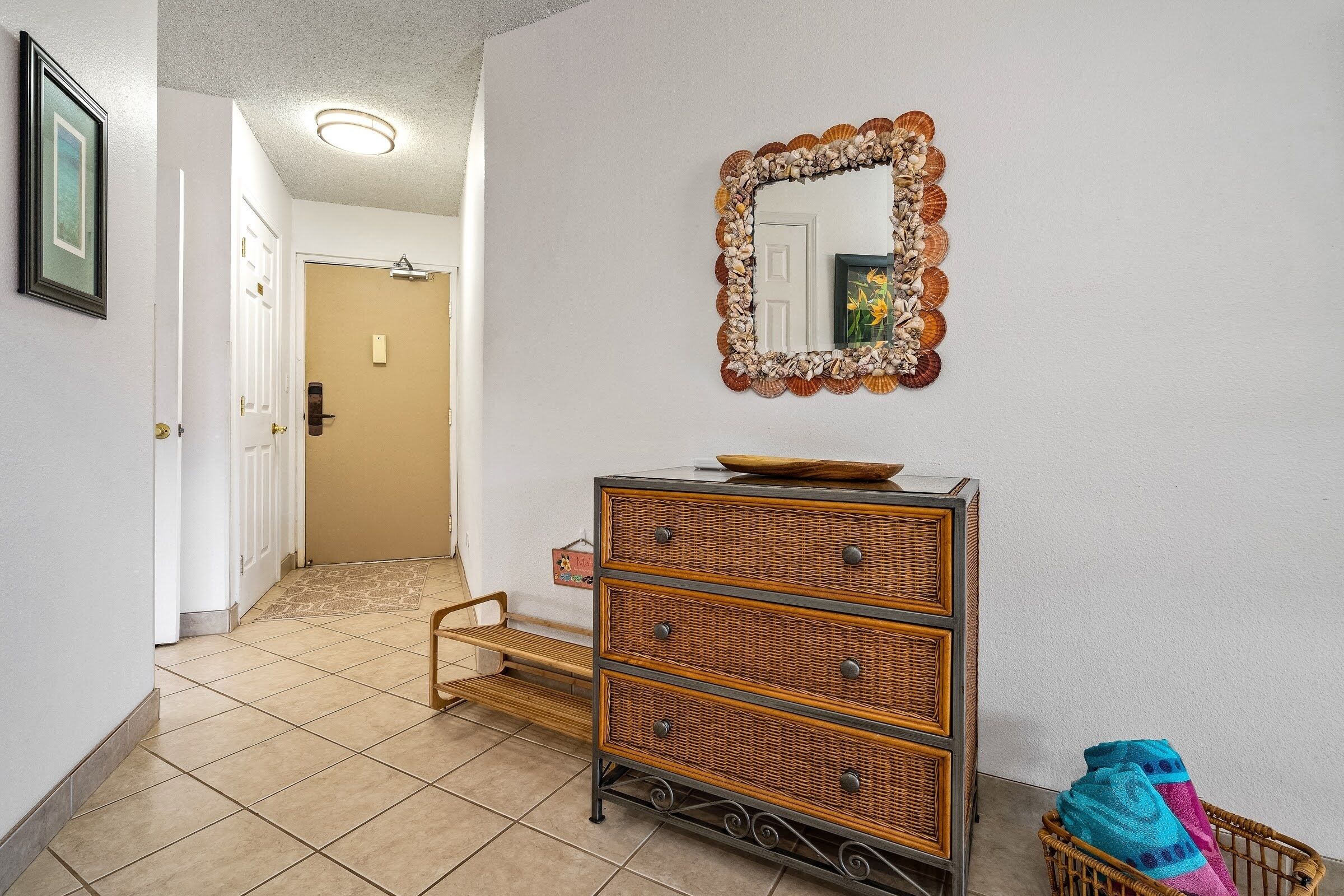 Un couloir avec une commode en osier, un miroir décoratif et une porte donnant sur une autre pièce.