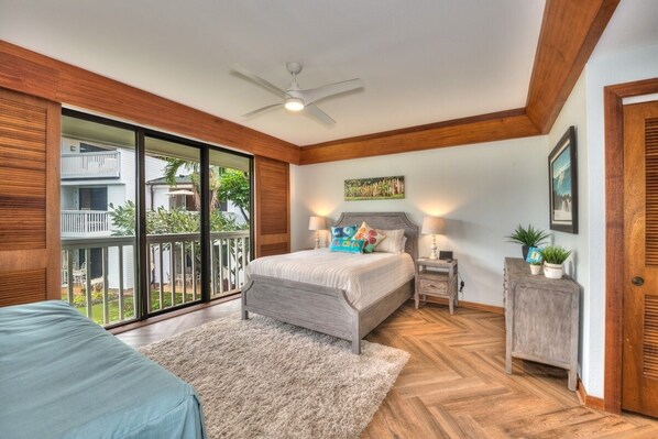 A bedroom with a large bed, a ceiling fan, a wooden floor, and a view of a balcony.