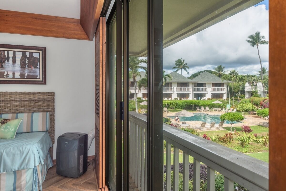 A balcony with a view of a swimming pool, palm trees, and a building in the background.