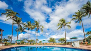 A swimming pool surrounded by palm trees and lounge chairs, with a clear sky above.