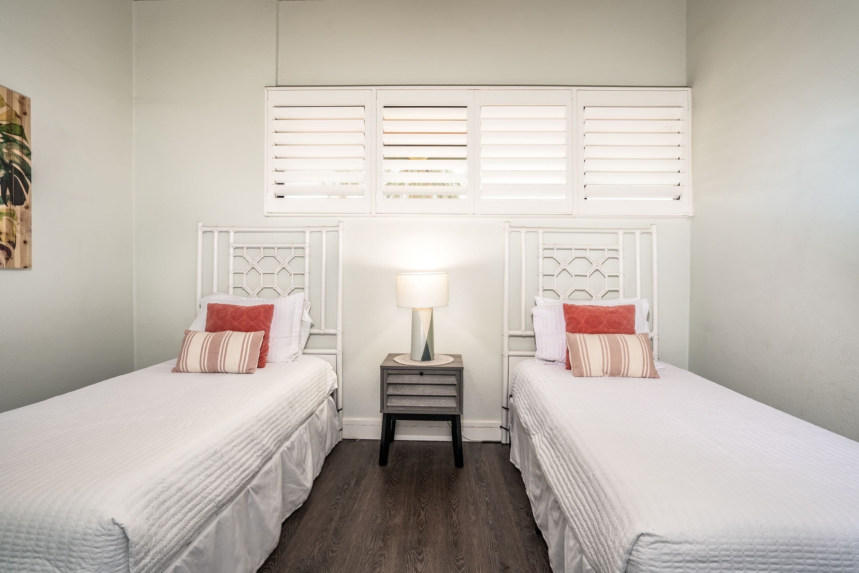 A bedroom with two beds, a nightstand with a lamp, and a window with shutters.