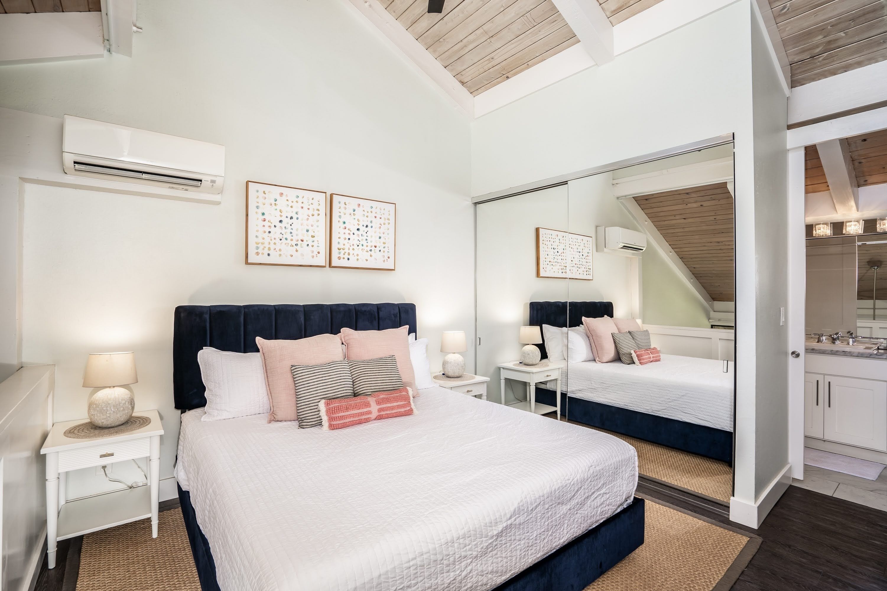 A modern bedroom with a large bed, bedside tables, a mirror, and an air conditioning unit.
